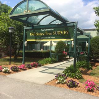 The entrance to a facility featuring a covered walkway and vibrant flower beds.