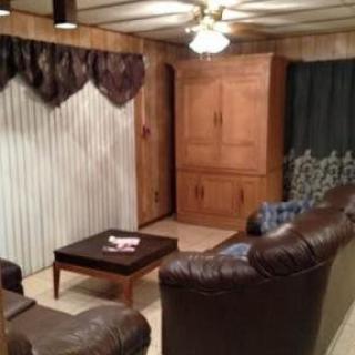 A cozy living room with leather sofas, a wooden coffee table, wood-paneled walls, and a ceiling fan.