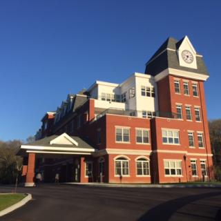 A modern brick hospital building bathed in sunlight under a clear blue sky.