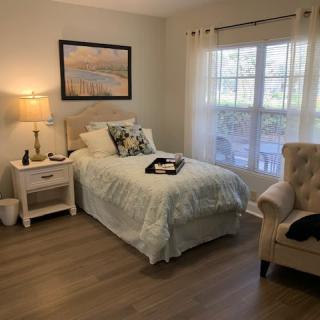 A cozy bedroom with a single bed, nightstand, and armchair by the window.