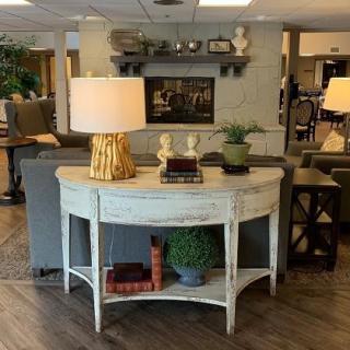 A cozy living room setup featuring a distressed console table with a lamp, books, and decorative plants.
