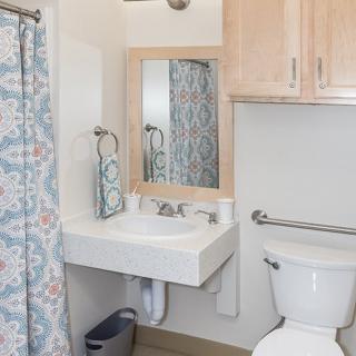 A clean and organized bathroom with a modern design, featuring a sink, toilet, mirror, and floral shower curtain.