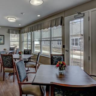 A well-lit dining area with tables and chairs arranged near large windows.