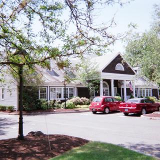 A suburban house with a front driveway, two parked cars, and surrounding trees.