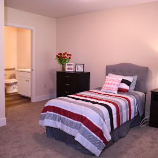 A cozy bedroom featuring a single bed with a colorful striped blanket, complemented by bedside tables and decorative flowers.
