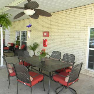 An outdoor patio with a dining set, including a table and chairs with red cushions, accompanied by a ceiling fan and decorative plants.