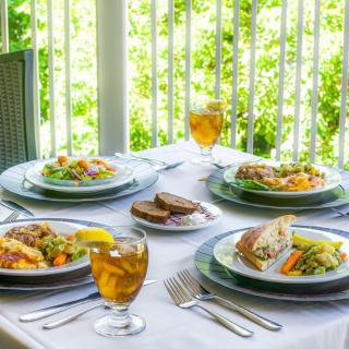 Outdoor dining setup featuring salads, sandwiches, and iced tea on a sunny patio.
