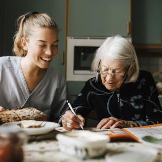 A caregiver assisting an elderly woman with writing at home.