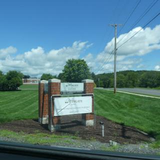A roadside sign set against a backdrop of green grass and a bright blue sky.