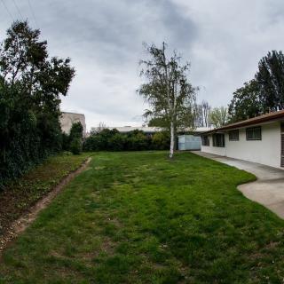A backyard with a grassy area, surrounded by trees and a house under a cloudy sky.