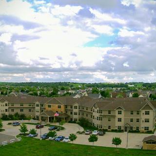 A spacious residential building surrounded by lush greenery and dotted with clouds in the sky.