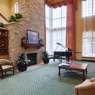 A spacious living room with a grand piano, stone fireplace, and tall windows.