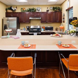 A modern kitchen with stainless steel appliances and orange chairs at the countertop dining area.