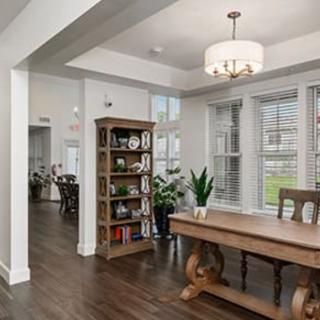 A cozy dining room featuring a wooden table, bookshelf, and large windows.