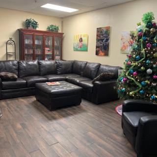 A cozy living room decorated for the holidays with a large black sectional sofa and a vibrant Christmas tree.