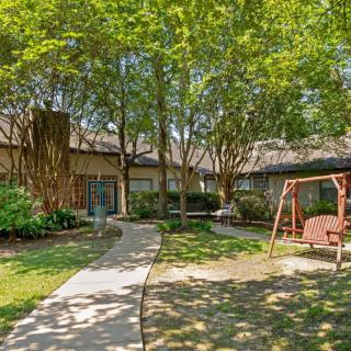 A tranquil garden area with a pathway, surrounded by trees and featuring a wooden swing set.