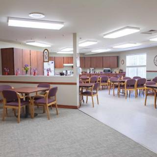 A spacious dining area with multiple tables and chairs, connected to a kitchen space.
