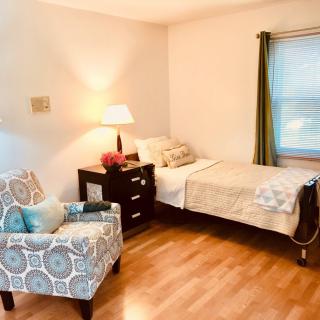A cozy bedroom with a single bed, armchair, and nightstand under warm lighting.