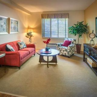 A cozy living room with a red sofa, floral armchair, and a central coffee table under warm lighting.