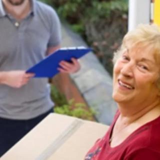 An elderly woman receives a package with a smile as a delivery person holds a clipboard.