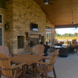 A cozy outdoor patio with wooden furniture, a stone fireplace, and a mounted TV.
