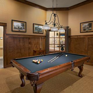 A well-appointed billiard room featuring a classic pool table, elegant wood paneling, and a stylish chandelier.