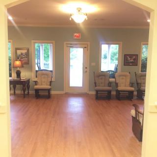 A cozy waiting room with a wooden floor and several chairs arranged along the walls.