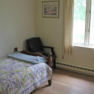 A simple bedroom with a single bed, chair, and window with curtains.