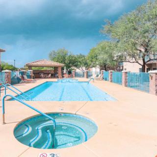 An outdoor swimming pool and hot tub surrounded by a fence, with trees in the background under a bright sky.