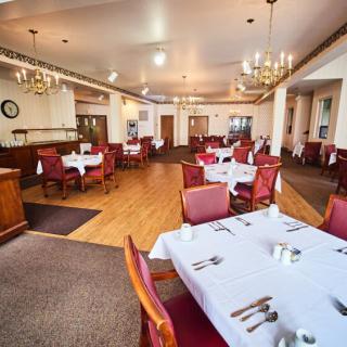 A spacious restaurant dining area with neatly arranged tables and chairs, adorned with chandeliers and white tablecloths.