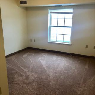 An empty room with carpet flooring and a single window.