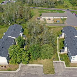 Aerial view of a residential complex surrounded by greenery and an adjacent parking area.