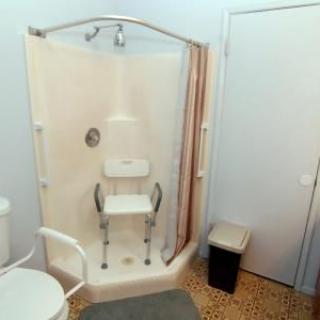 An accessible bathroom featuring a shower with a safety chair and rail.