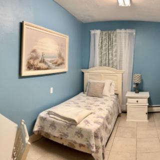A cozy bedroom with blue walls, featuring a single bed, a nightstand, and a decorative painting.