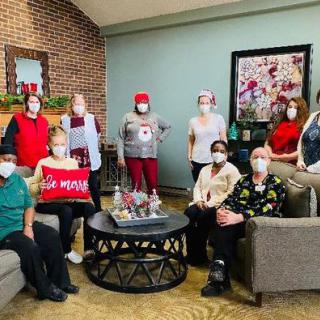 A group of people gathered indoors wearing festive clothing and masks, surrounded by holiday decorations.