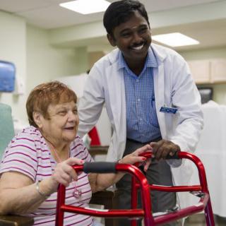 A healthcare professional assisting an elderly woman with a walker in a nursing home setting.