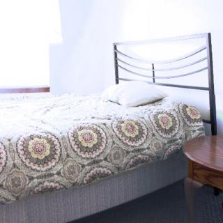 A neatly made bed with a patterned bedspread and a single pillow, next to a round wooden side table.