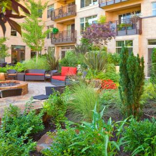 A vibrant urban garden with lush greenery and comfortable outdoor seating in an apartment complex.