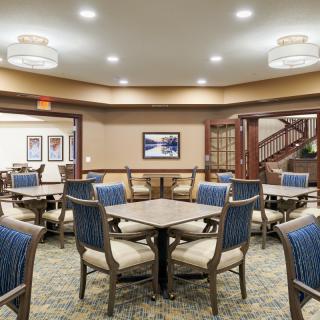 A well-lit dining area with tables and chairs arranged neatly, featuring elegant lighting and a carpeted floor.