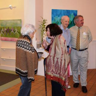 A group of people engaging in conversation at an art gallery event with paintings displayed on the walls.