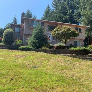 A two-story house surrounded by trees and a grassy lawn on a sunny day.