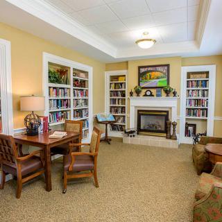 A cozy living room with bookshelves and a fireplace, featuring a table and chairs for lounging.