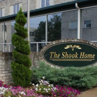 Entrance of The Shook Home with surrounding greenery and flowers.