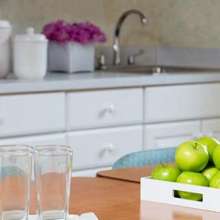 A kitchen counter with a tray of green apples, glasses, and decorative flowers.