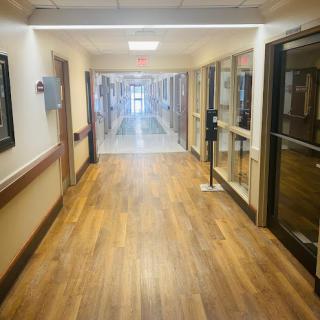 A well-lit hallway in a healthcare facility, featuring wooden flooring and glass-paneled doors.