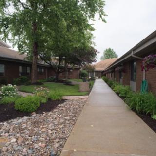 A landscaped sidewalk between buildings with lush greenery and trees.