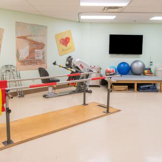 A well-equipped physical therapy room with parallel bars and exercise equipment.