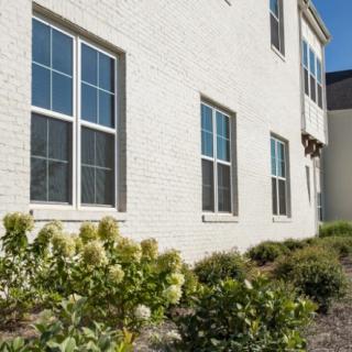A side view of a brick house with windows and a landscaped garden on a sunny day.