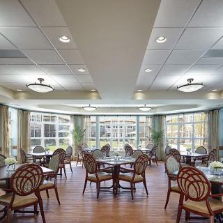 A spacious dining area with multiple tables and chairs, featuring large windows that allow natural light to pour in.