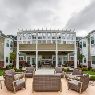 An outdoor patio area featuring comfortable seating under a pergola, surrounded by a well-maintained building and landscaping.